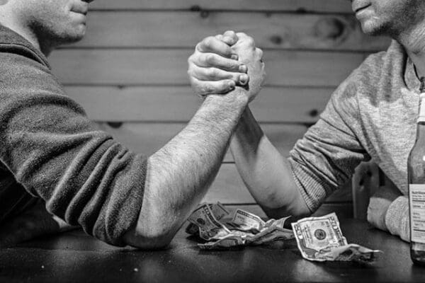 Two men arm wrestling on a table with cash