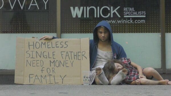 Homeless man with sleeping daughter holds a sign to seek money