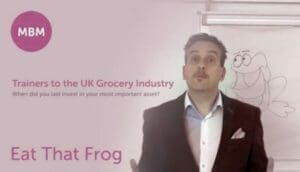 Man standing in front of an image of a frog with 'Eat That Frog' written behind him