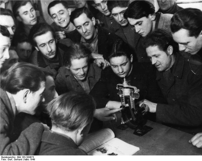 Black and white photo of a man teaching a group of men how to use a scientific instrument