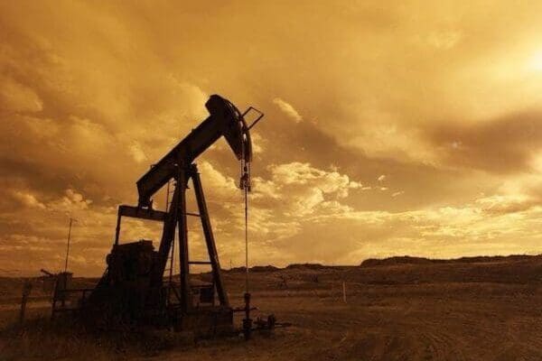 Oil well pump in middle of field with cloudy sunset sky
