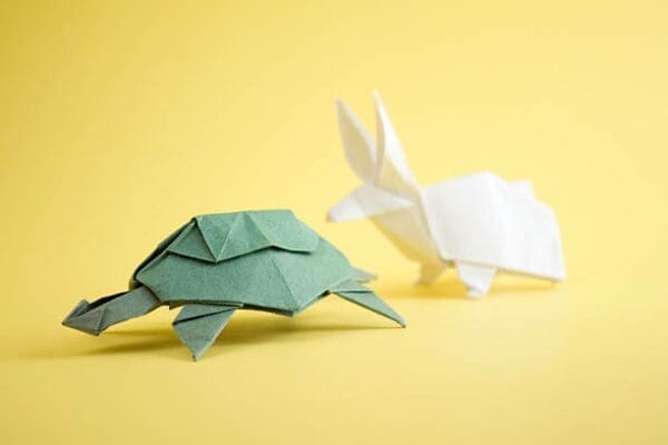 Origami green paper tortoise and white hare on yellow background