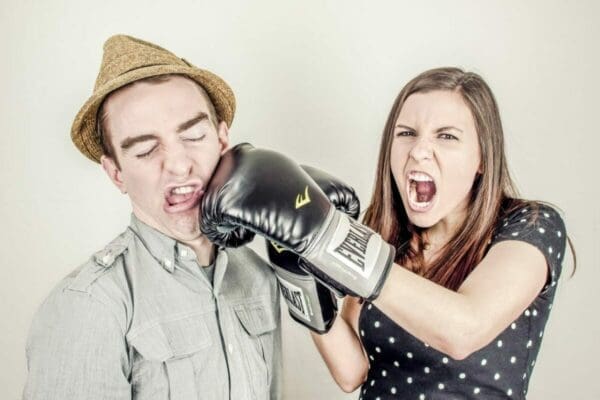 Angry woman punching a man with boxing gloves on