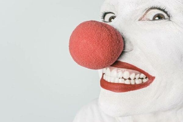White painted face with a large red nose and red lips smiling and white background