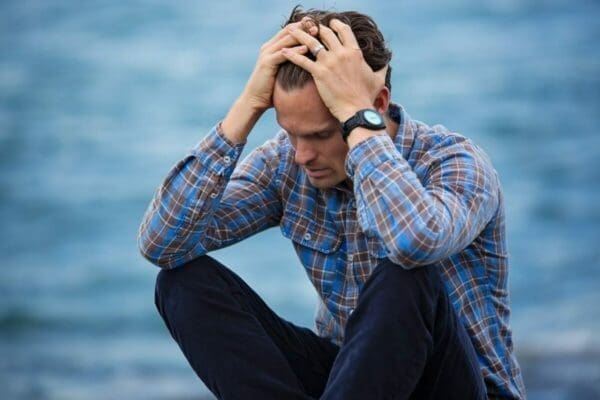 Man stressed by poor mental health has his hands on his head with sea in the background