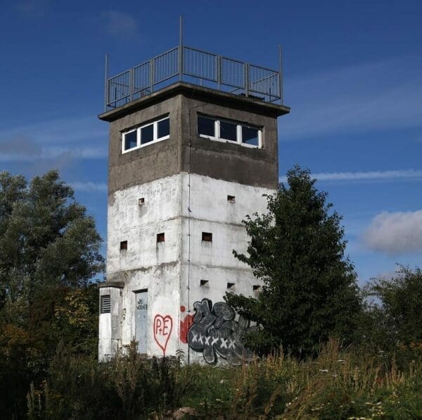 Run down watch tower with graffiti on it and tall trees and blue sky background