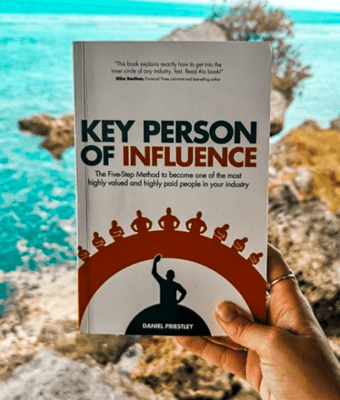 Key Person of Influence book by Daniel Priestley held in a hand with an ocean background