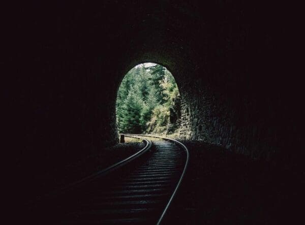 Railway inside a dark tunnel leading to an exit of light and trees