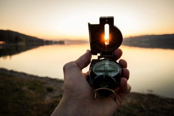Man holding a compass in front of a lake on a sunset