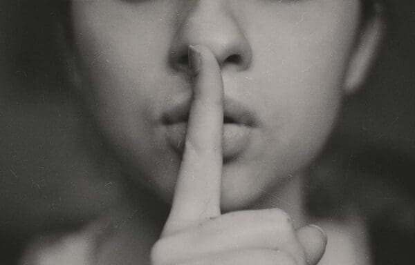 Lower portion of girl's face with index finger on her lips signalling to be quiet