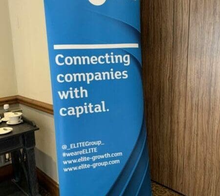 Blue standing sign outside a conference room with Elite logo and connecting companies with capital message