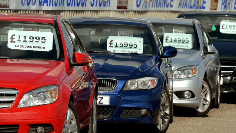 New cars lined up in an auto shop with prices in pounds posted on the windshields