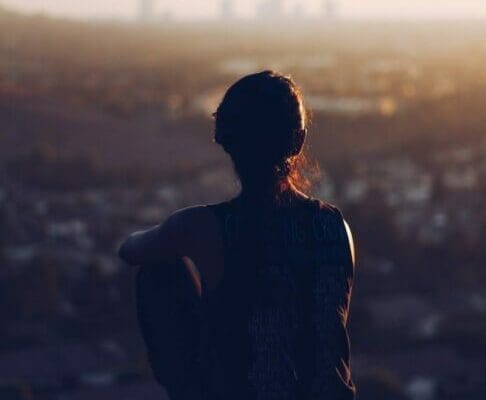 Back or woman sitting on a cliff looking out over a city