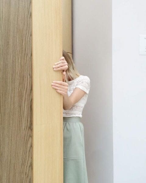 Shy woman hiding her face behind a wooden panel at work