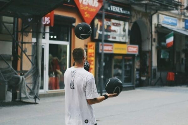 Man juggling three black balls in the middle of the street represents multi-tasking