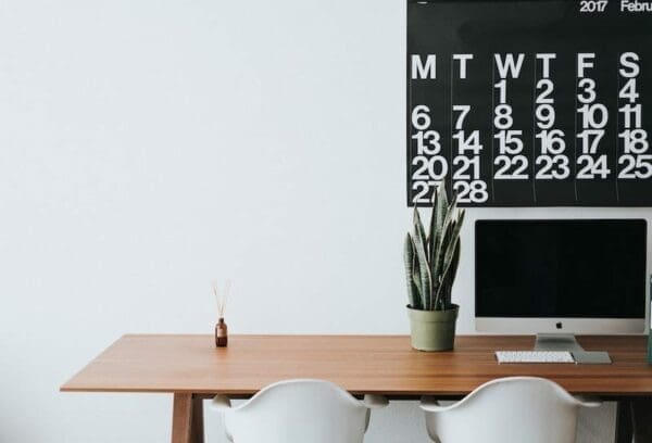 An iMac and a plant on top of a clean desk with a large calendar represents work from home space
