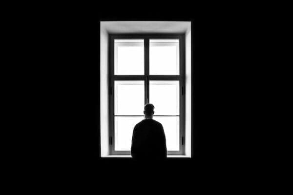 Silhouette of a man looking out of a window from a dark room