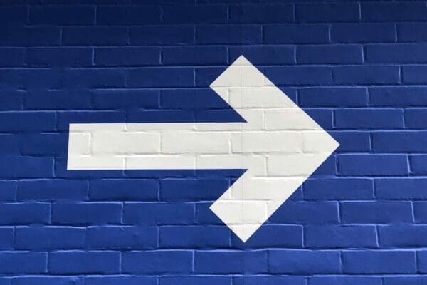 White arrow pointing to the right on a blue brick wall