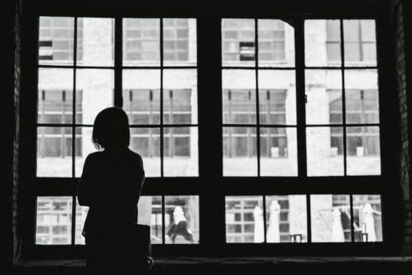 Silhouette of a woman looking out of big window is isolated and it affects her mental wellbeing