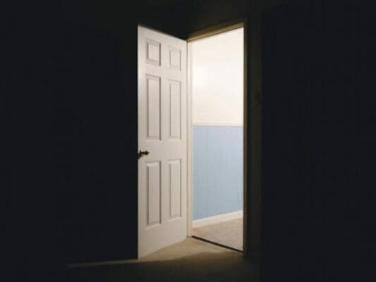 A dark room with an open door and light coming through 