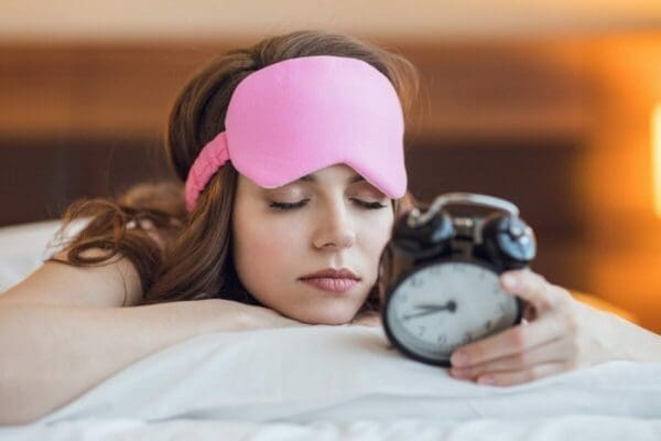 Woman asleep with an eye mask and holding an alarm clock is rested for better team collaboration
