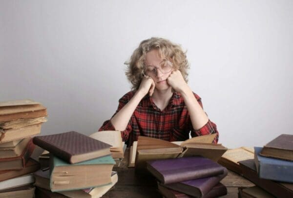 Woman surrounded by piles of books with her hands at her jaw is overwhelmed from too much to read