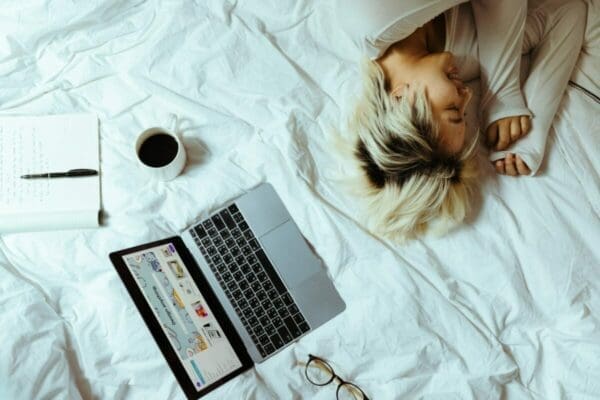 Woman asleep on her bed surrounded by her laptop and coffee is procrastinating