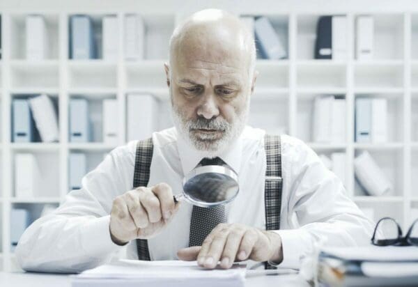 Businessman checking paperwork with a magnifier is checking its grammar