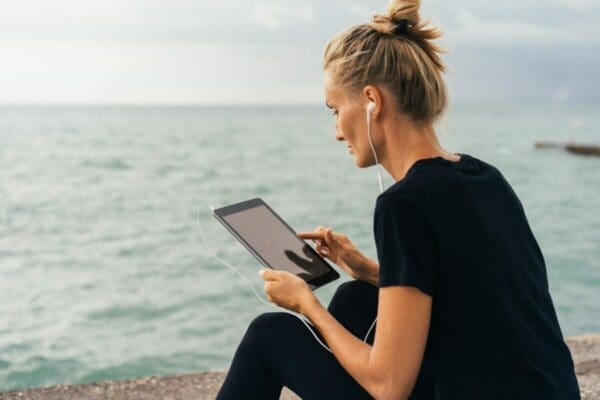 Woman sitting on the beach reading blog post on her tablet