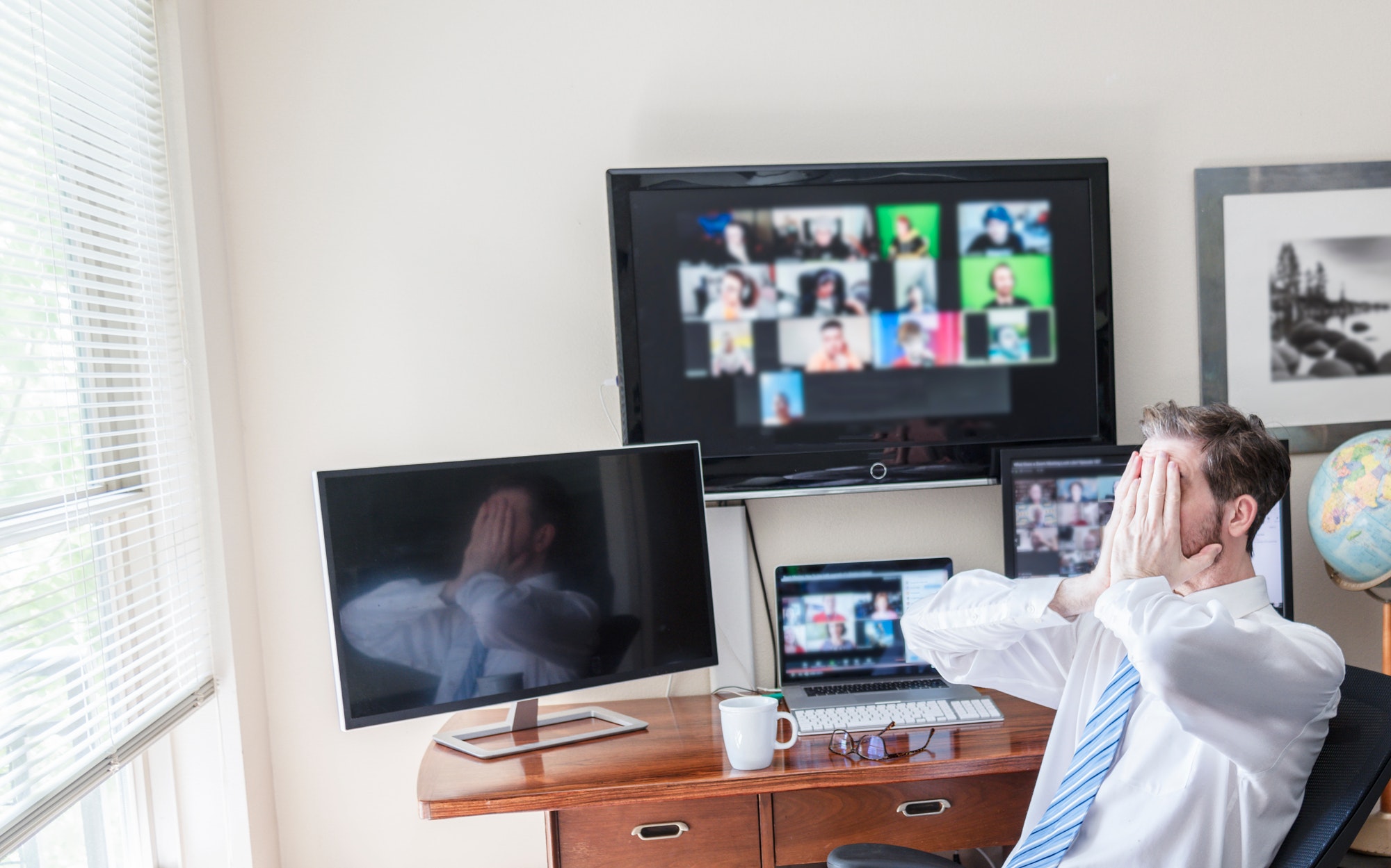 Man working with team via video chat, with heads in hands looking stressed