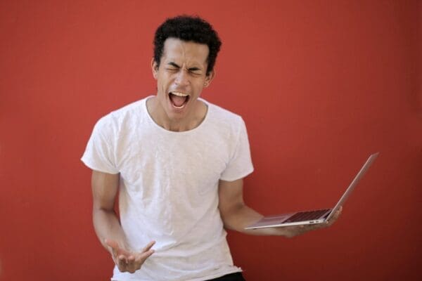 Frustrated man yelling with laptop in his hand with red background