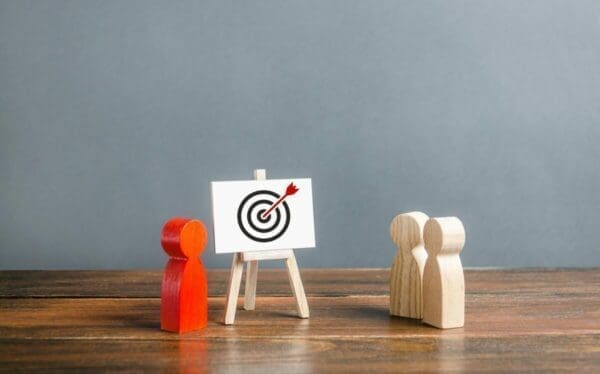 Three wooden figures looking at a bullseye on a whiteboard