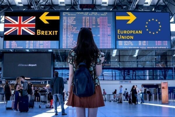 Woman standing in an airport between a European Union flag pointing right and Brexit British flag pointing left