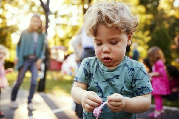Toddler boy unwrapping a lollipop in a park outdoors