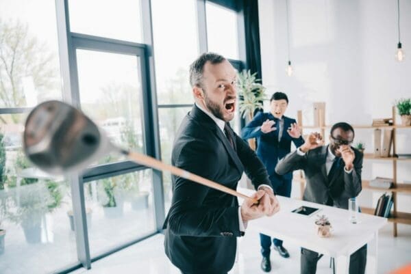 Angry manager swinging a golf club whilst other workers look scared