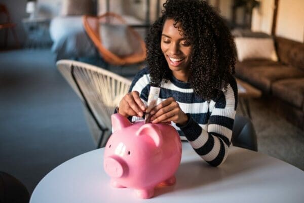 A Generation Z woman putting money into a pink piggy bank for financial security 