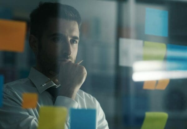 Businessman looking at sticky notes on a wall and looking for a solution