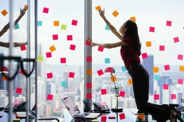 Woman standing on desk, attaching sticky notes to window