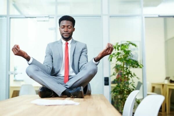 Businessman seated on the table in a yoga pose 