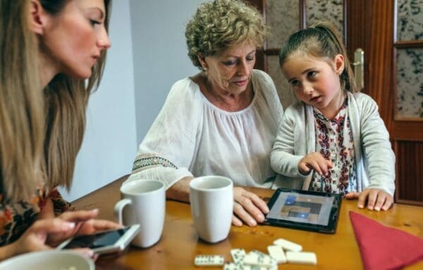 Little girl asking her mother and grandmother to buy her something on a tablet
