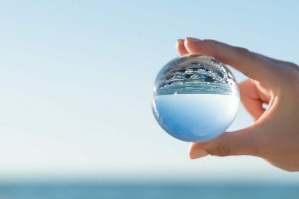 Hand holding a clear ball with a reflection of the sea in it