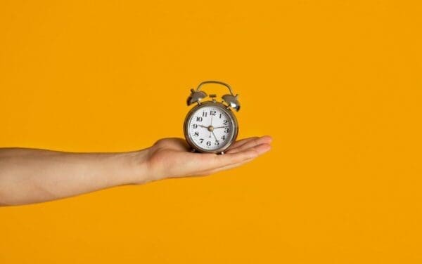 A hand holding an alarm clock on an orange background