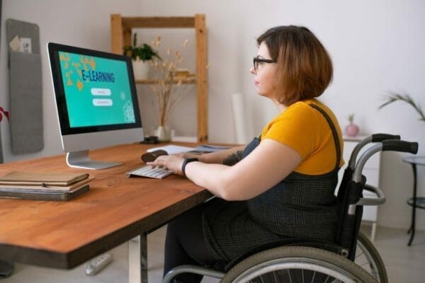 Disabled lady in a wheelchair does E-learning on her Mac computer
