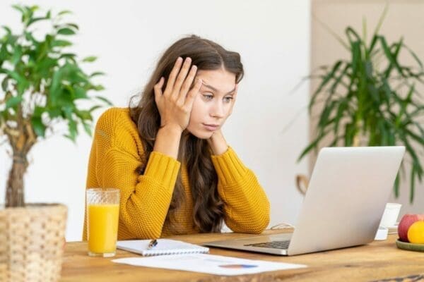 Woman at her desk with her head in hands is stressed by emails