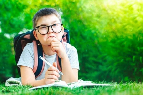 Young boy laying on grass with backpack is practicing calculations in his head