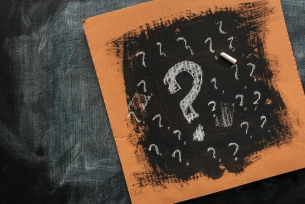 Sketched question mark on black painted cardboard represents meaning behind questions
