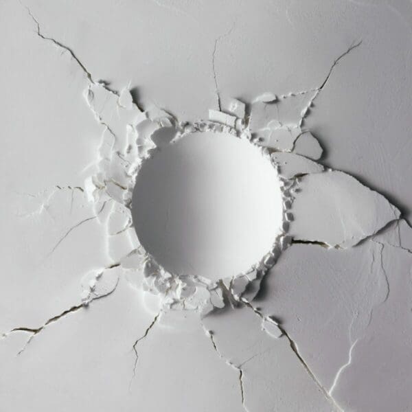 round indent in a white wall has surrounding cracks
