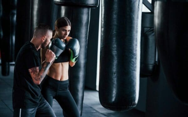 Tattooed boxing coach teaches young woman in the gym