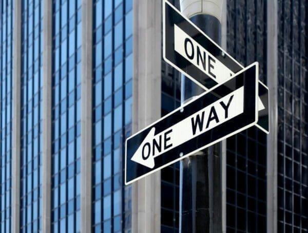 Two one way signs pointing opposite directions with a city organisation building in the background
