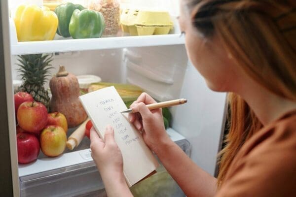 Female shopper checking shopping list with items in her fridge